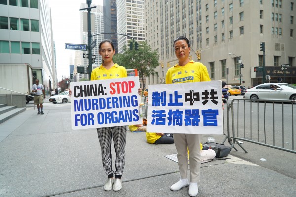 9月18日，山东潍坊法轮功学员葛云玲母子，在华尔道夫酒店对面马路上展示“制止中共活摘器官”标牌。（谢东延/大纪元）