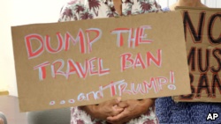 川普总统的批评者举着一块标语牌，呼吁撤销旅行禁令。（2017年6月30日）